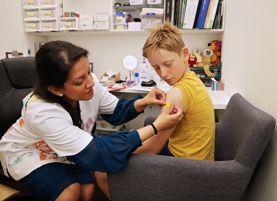 Health professional placing plaster on child after vaccination in consultation room 950x690