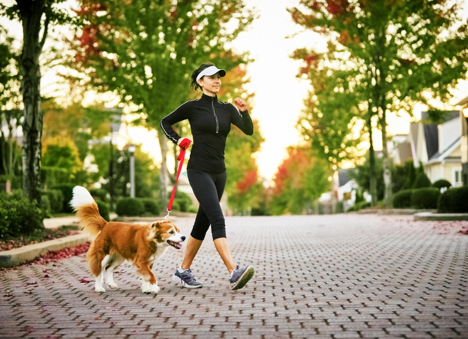 Woman walking dog wearing sun protective clothing 