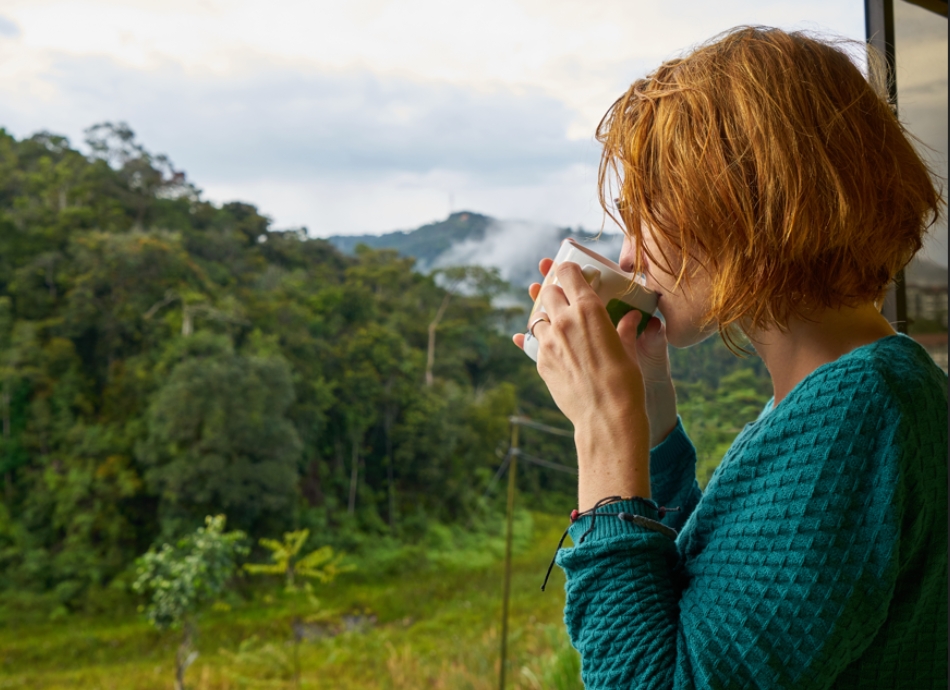 Young woman drinking tea and looking out to rural landscape